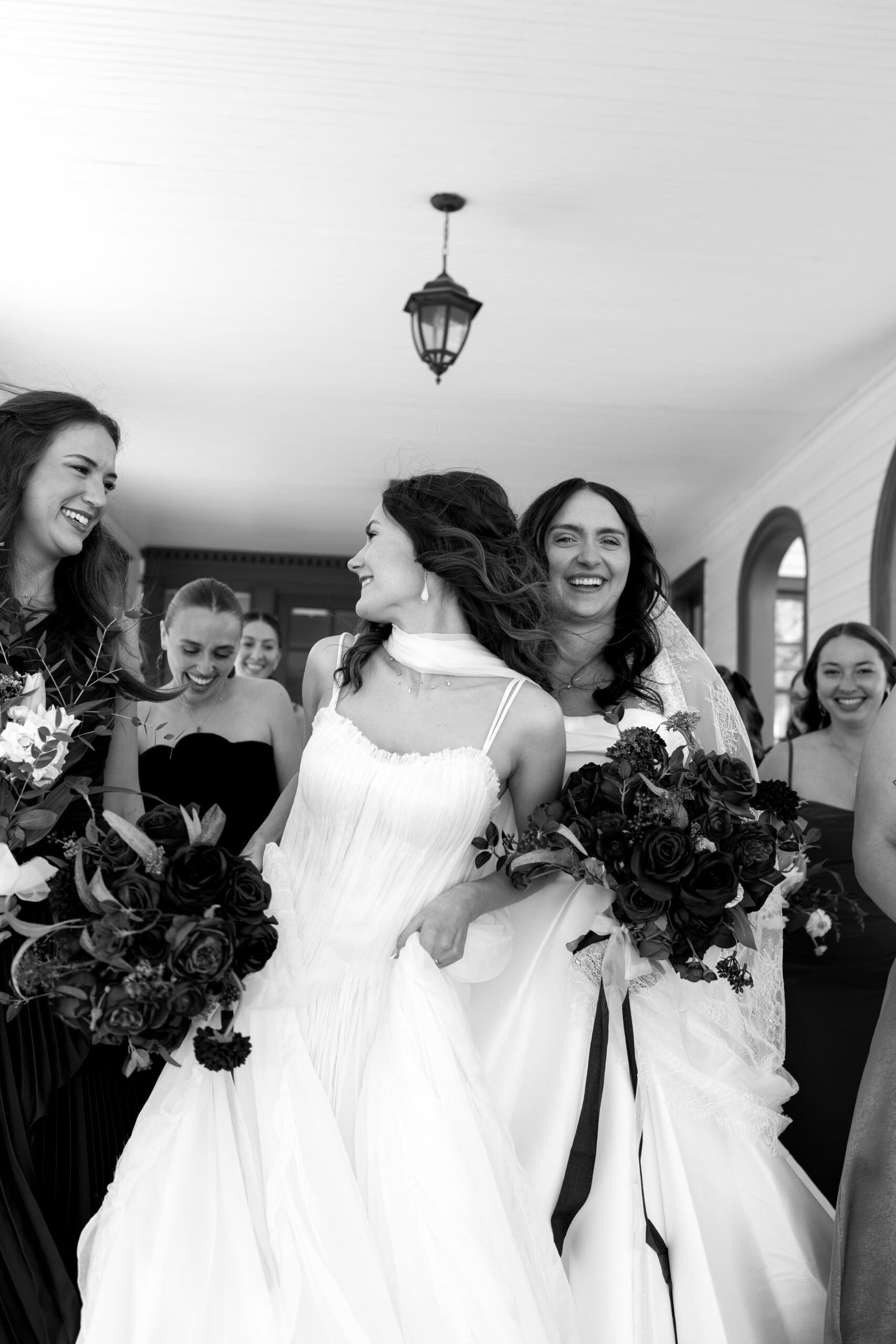 Two brides laughing with their bridesmaids in black and white